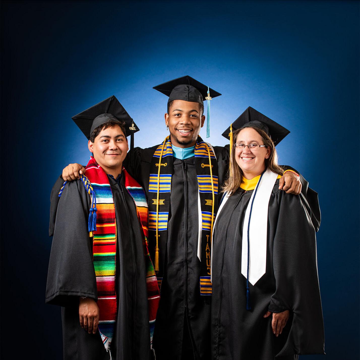 three students smiling at the camera in their cap and gown. 